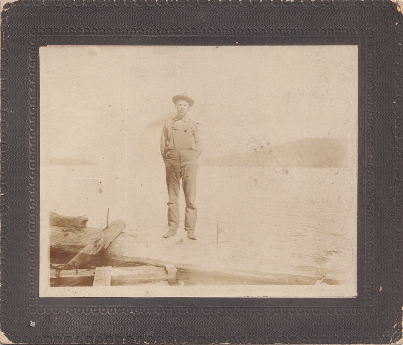Charlie Haushalter stands, hands in pockets, atop logs with Lake Coeur d'Alene in background